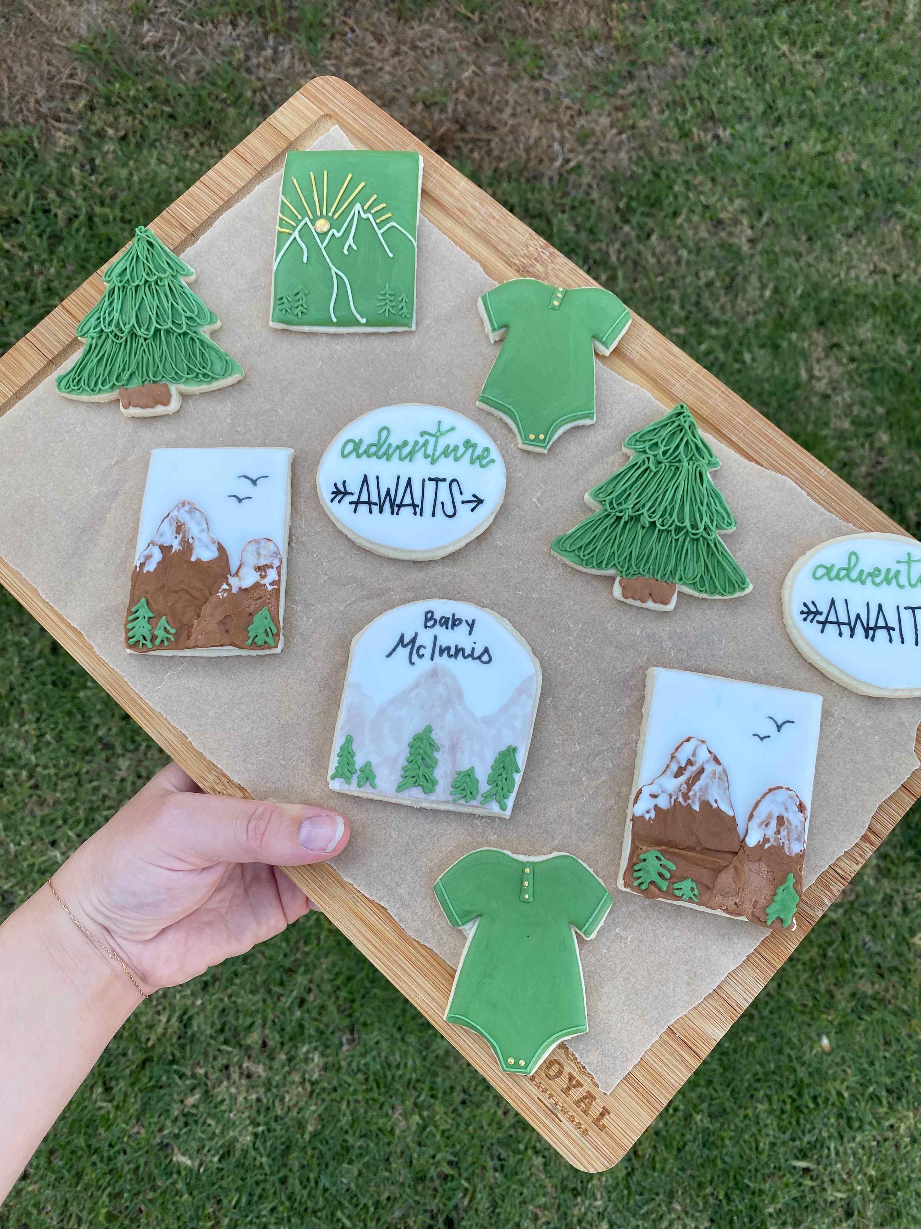 Adventure themed baby shower cookies with mountains, pine trees, and baby onesies